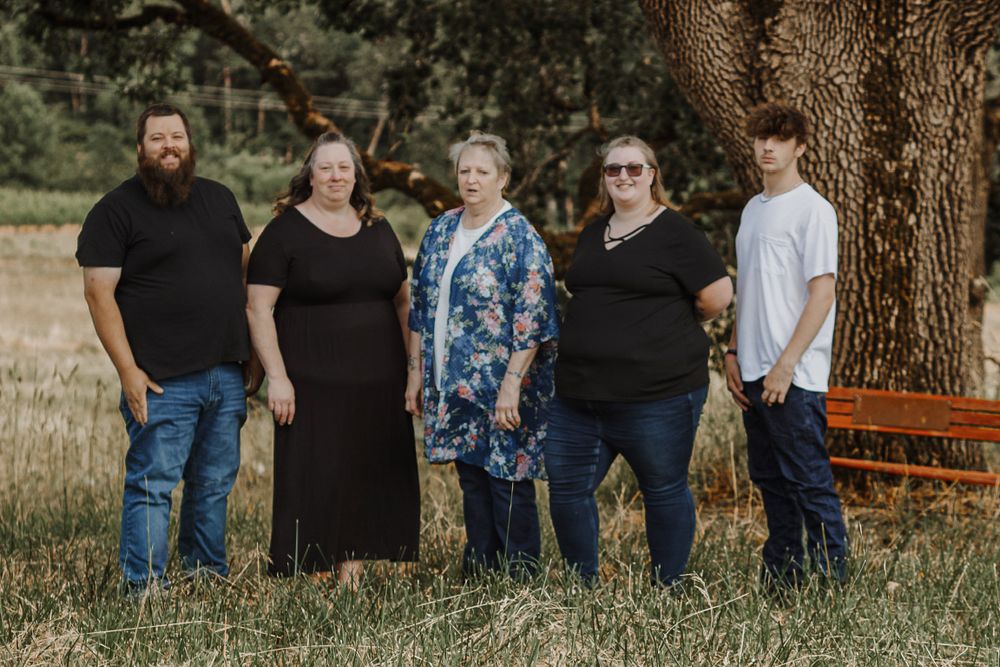 A family of five poses together under a large tree in a grassy outdoor setting.