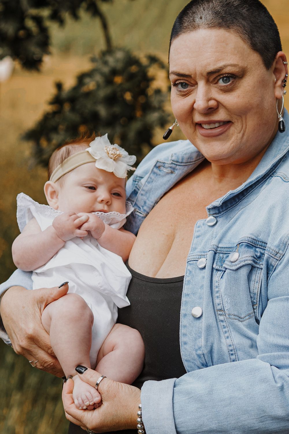 A woman tenderly holds a baby girl wearing a floral headband in an outdoor setting.