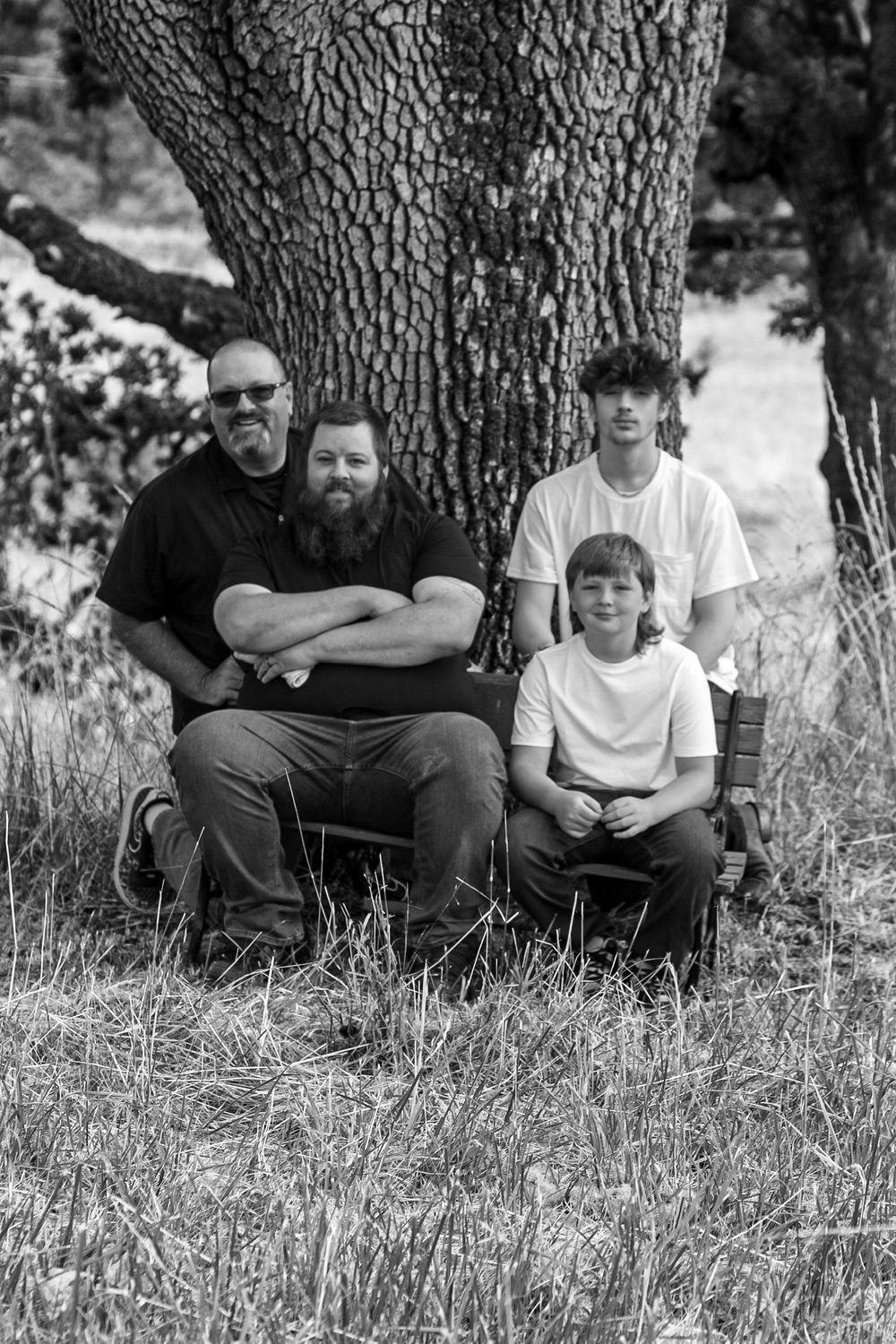 Black and white photo of four males posing together under a large tree in a grassy field.