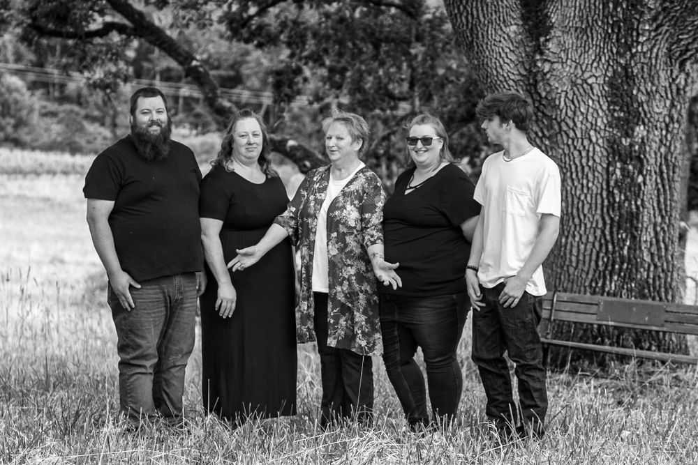 Black and white portrait of five adults standing together near a large tree in a field.