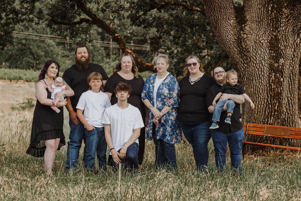 Large extended family group portrait standing together under a sprawling oak tree in a golden field.