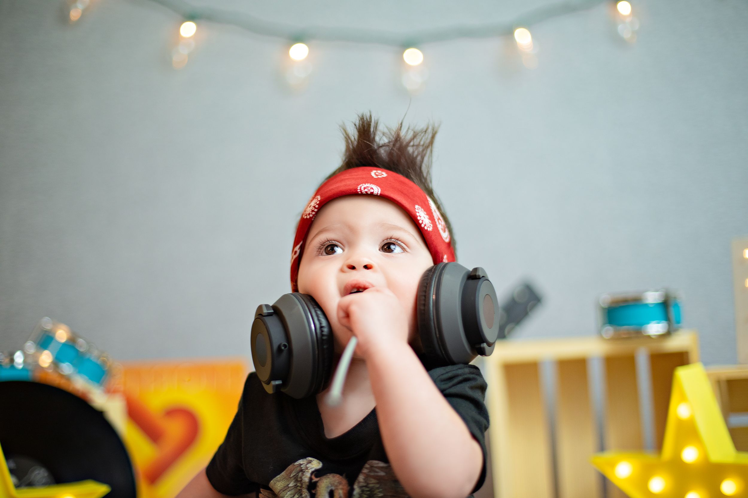 A child lies on the floor listening to music through large headphones under string lights.