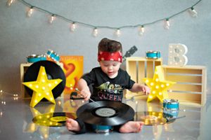 Small child playing with vinyl record against backdrop with star lights and string lights above.