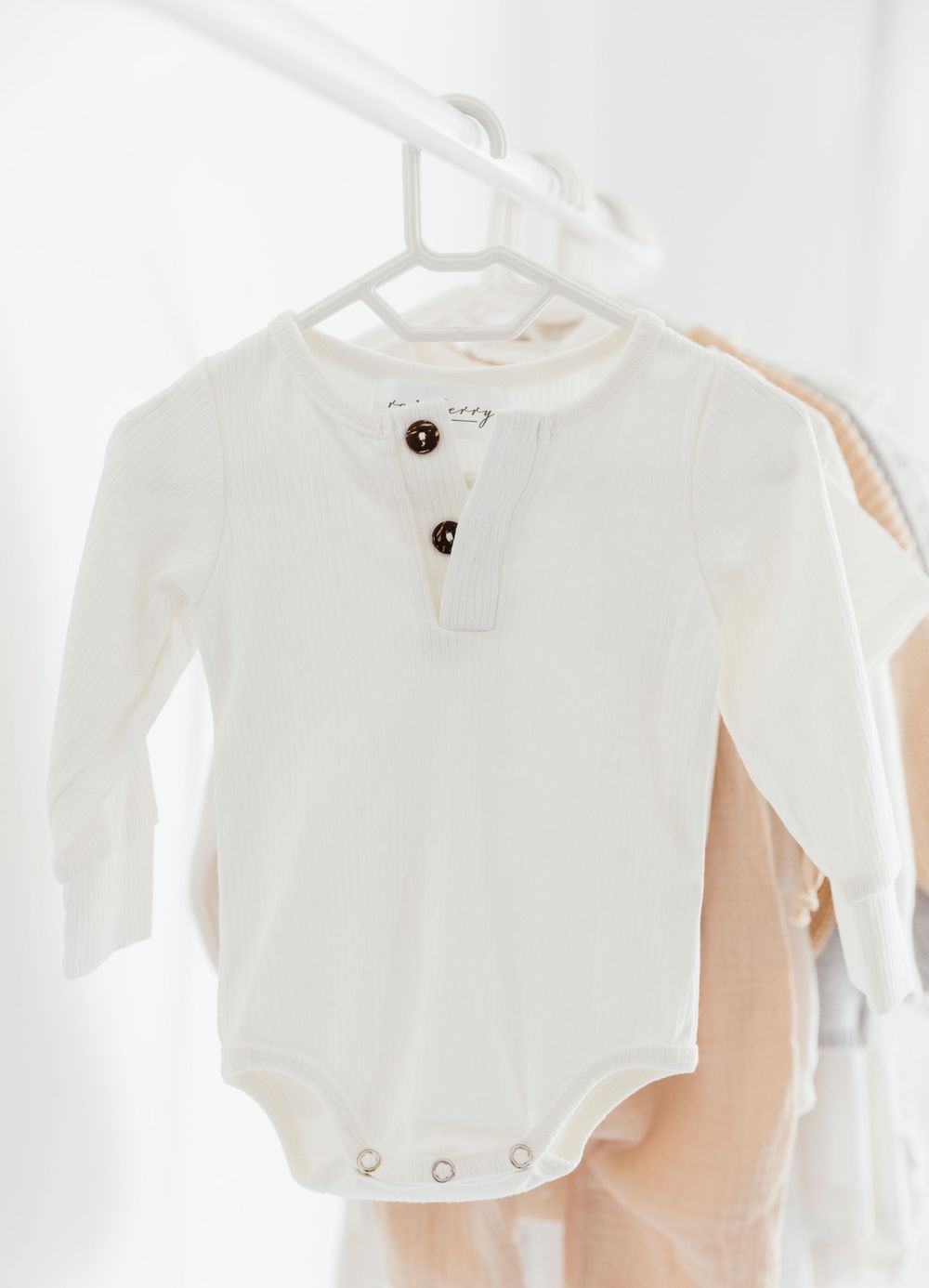 Classic white long-sleeve baby bodysuit with button placket hanging on white hanger.