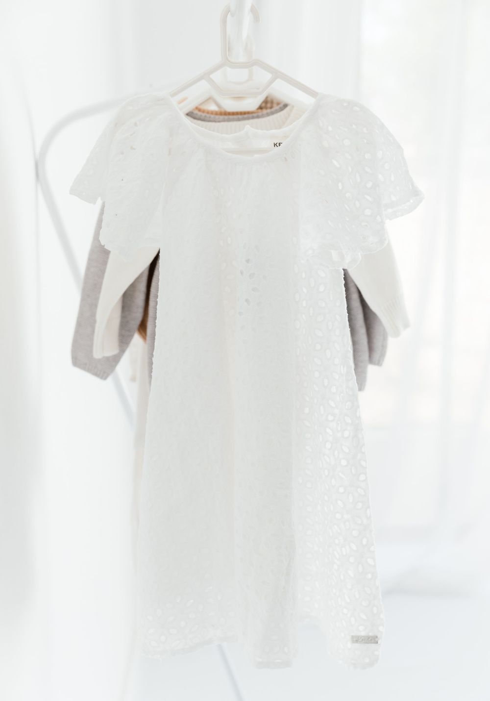 White lace or eyelet dress on a white plastic hanger hanging against a light background.