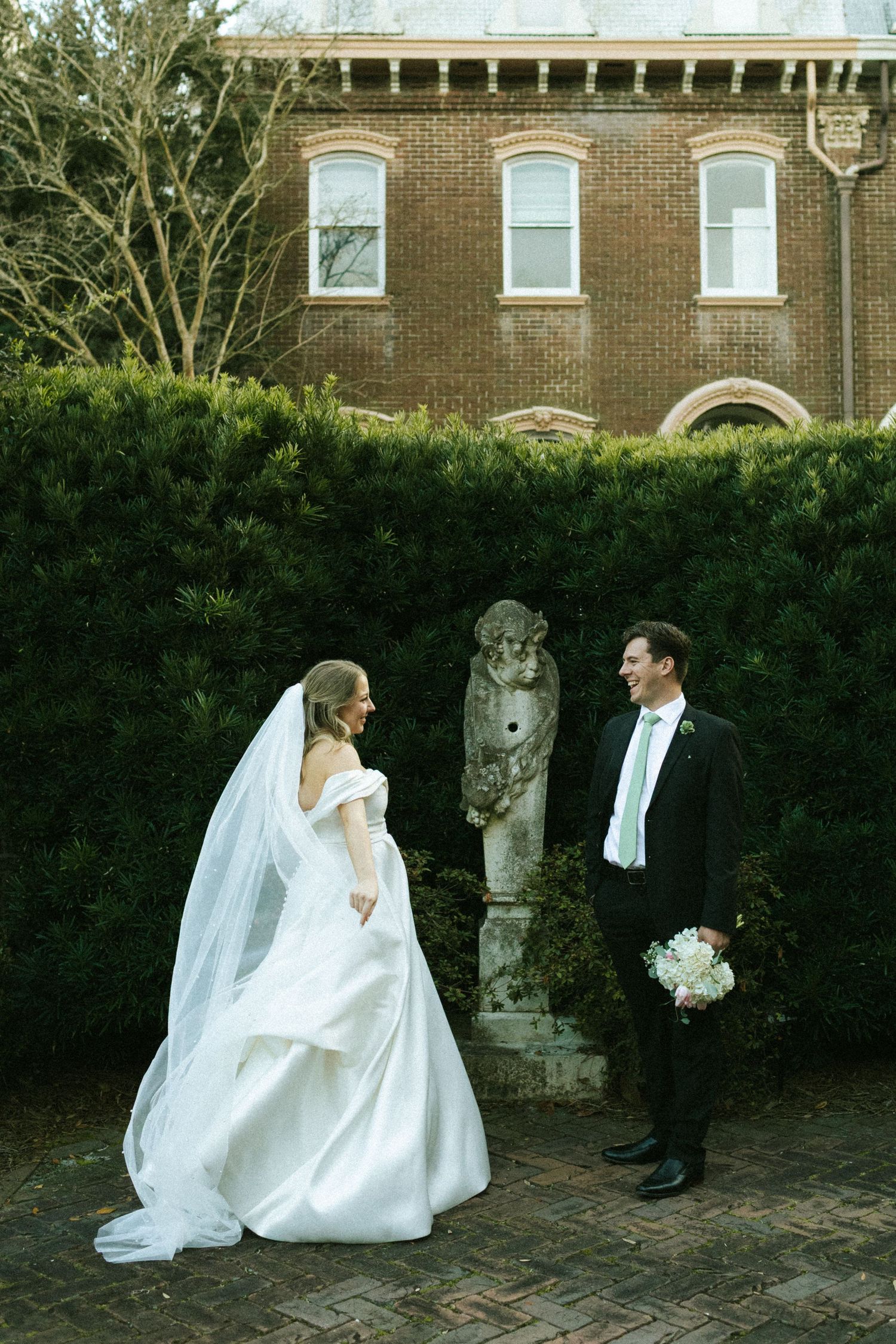 A bride and groom facing each other in the Harper Fowlkes House courtyard, she is swinging her dress and veil around her