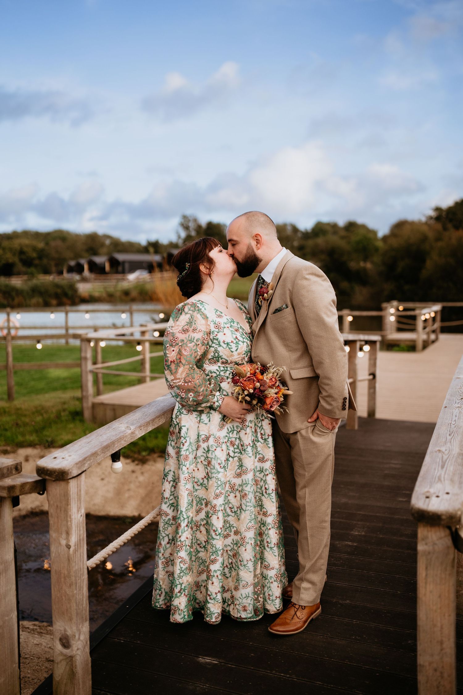 Newlywed couple embraces in a dreamy wildflower meadow, with the bride wearing an off-shoulder lace gown and flowing veil.