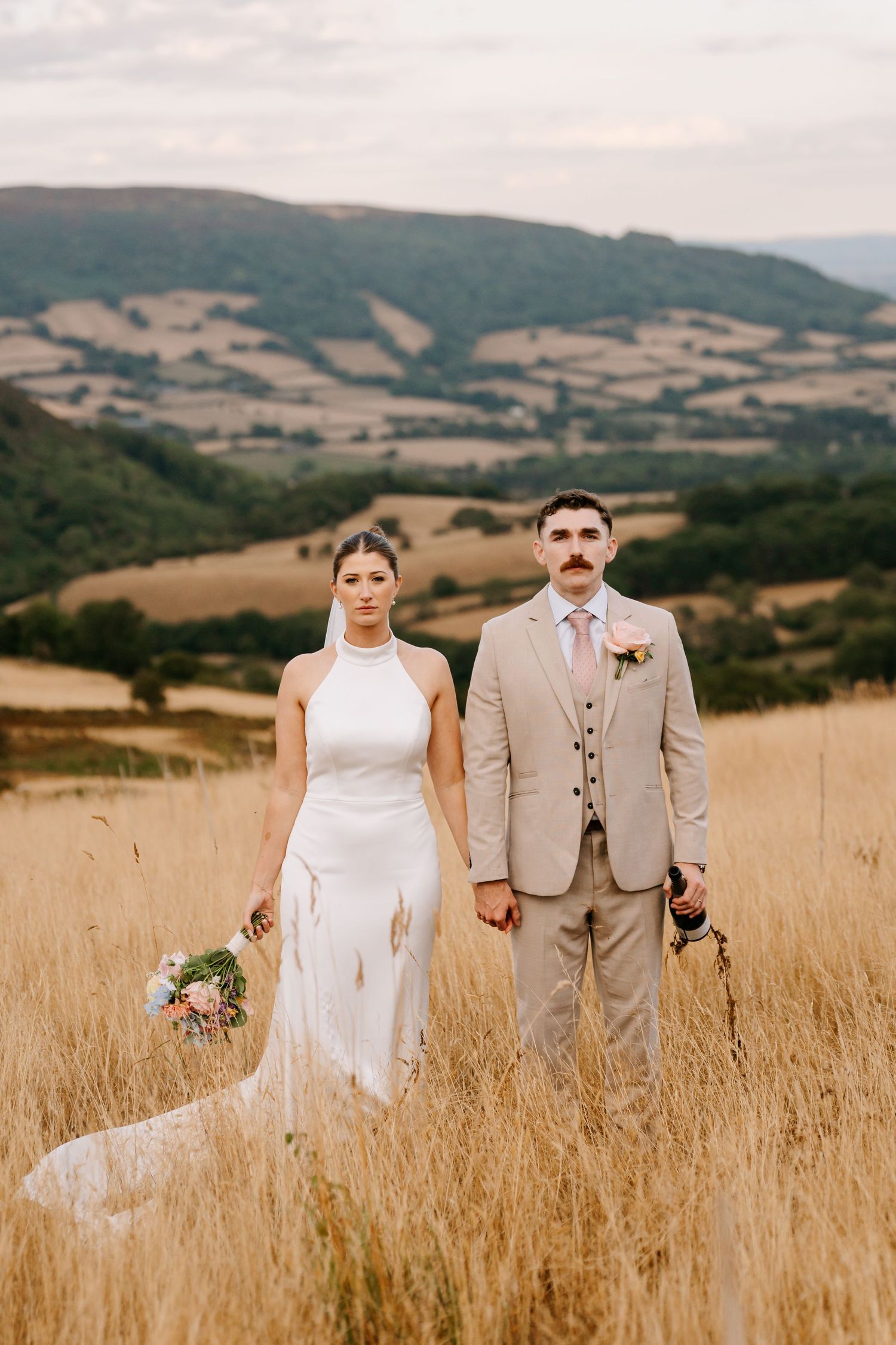 Newlywed couple embraces in a dreamy wildflower meadow, with the bride wearing an off-shoulder lace gown and flowing veil.