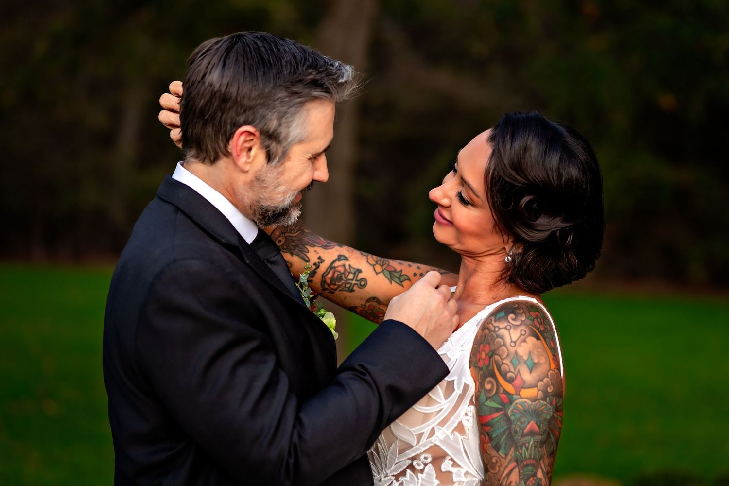 Close up of wedding couple embraces outdoors, showing lace dress details and tattoos in natural lighting.
