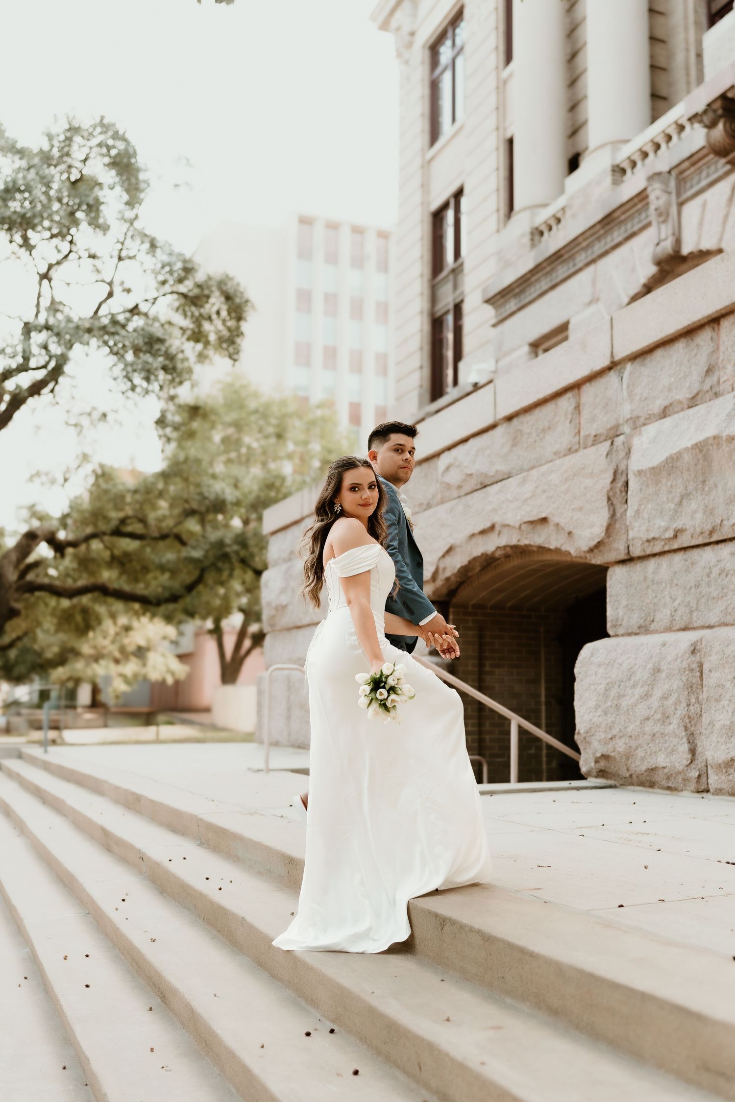 Bride in white dress posing on stone steps of historic building.