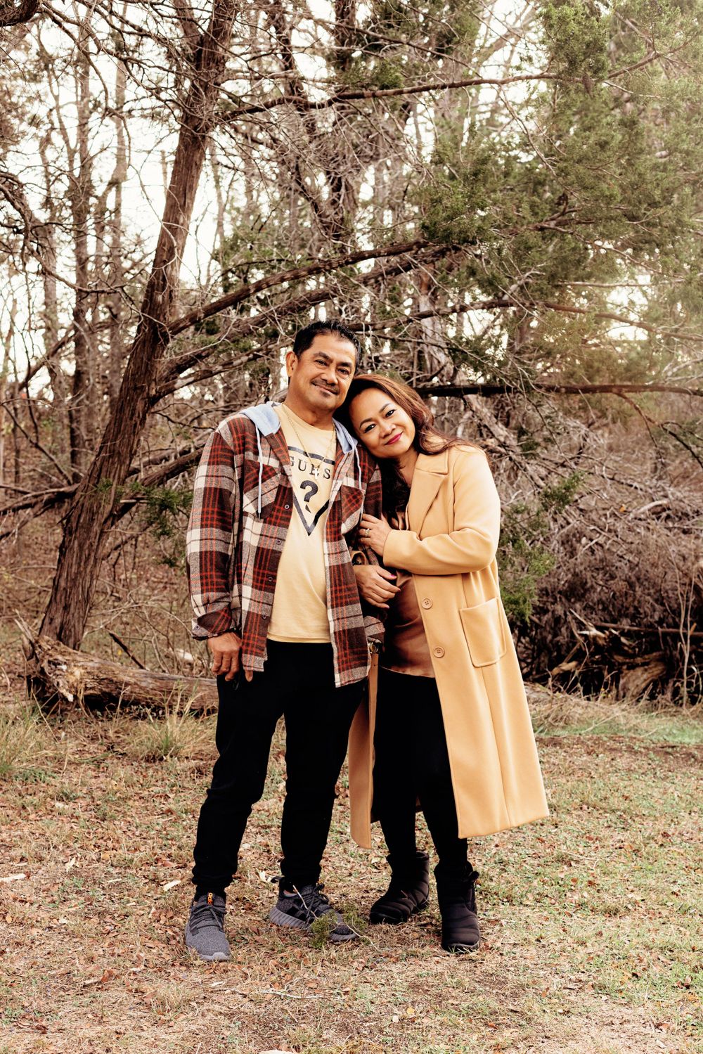 A couple shares a tender outdoor moment together in a wooded area, wearing casual fall attire.