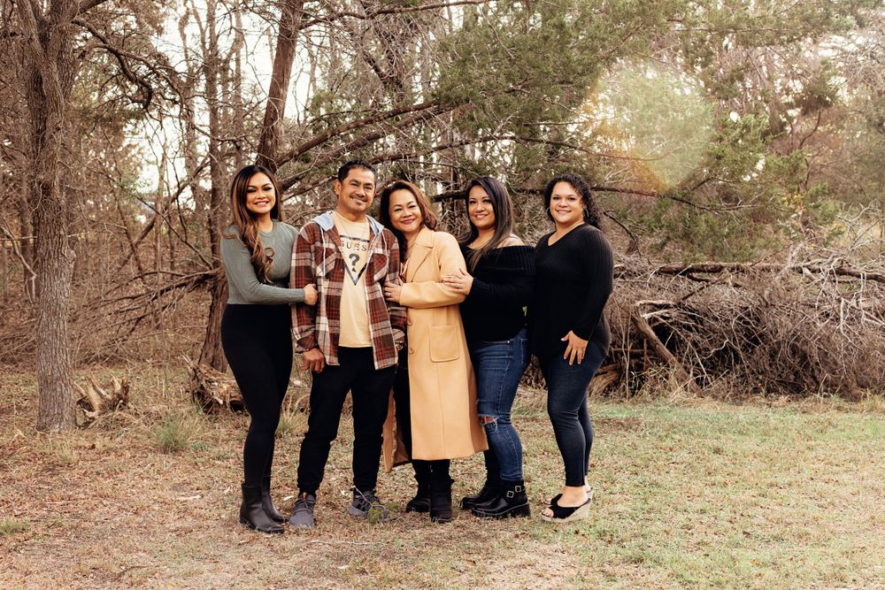 A group of 5 friends wearing fall outfits stand together outdoors with trees and brush in the background.