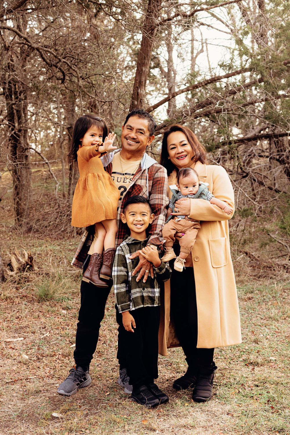 A family of five poses together in a wooded setting wearing coordinated casual outfits.