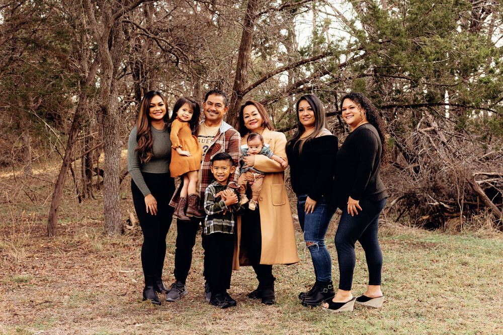 A group of women and children pose together outdoors in coordinated dark clothing and a tan coat.