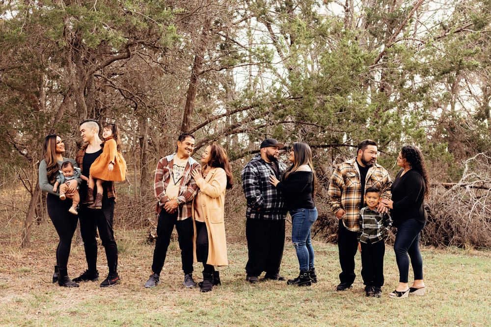 A group stands together in an outdoor wooded setting during a photo session on a fall day.
