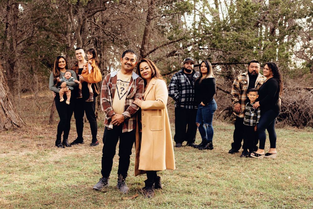 Several groups of friends standing together outdoors in casual attire on a grassy area near wooded trees.