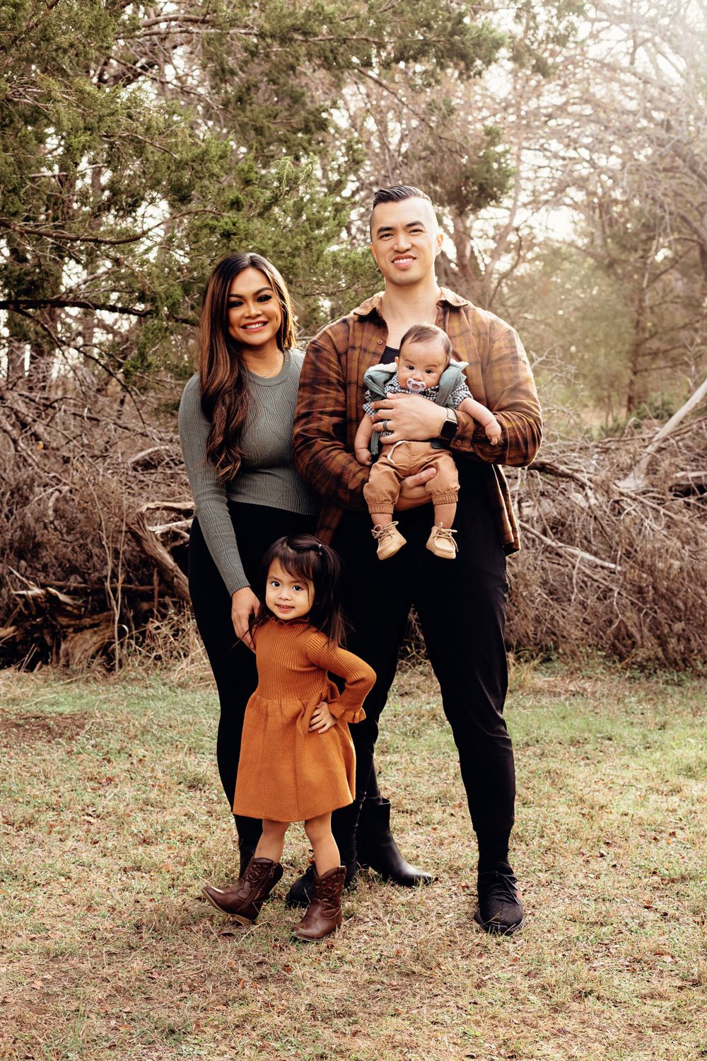 A family poses together for a portrait outdoors among trees during autumn.