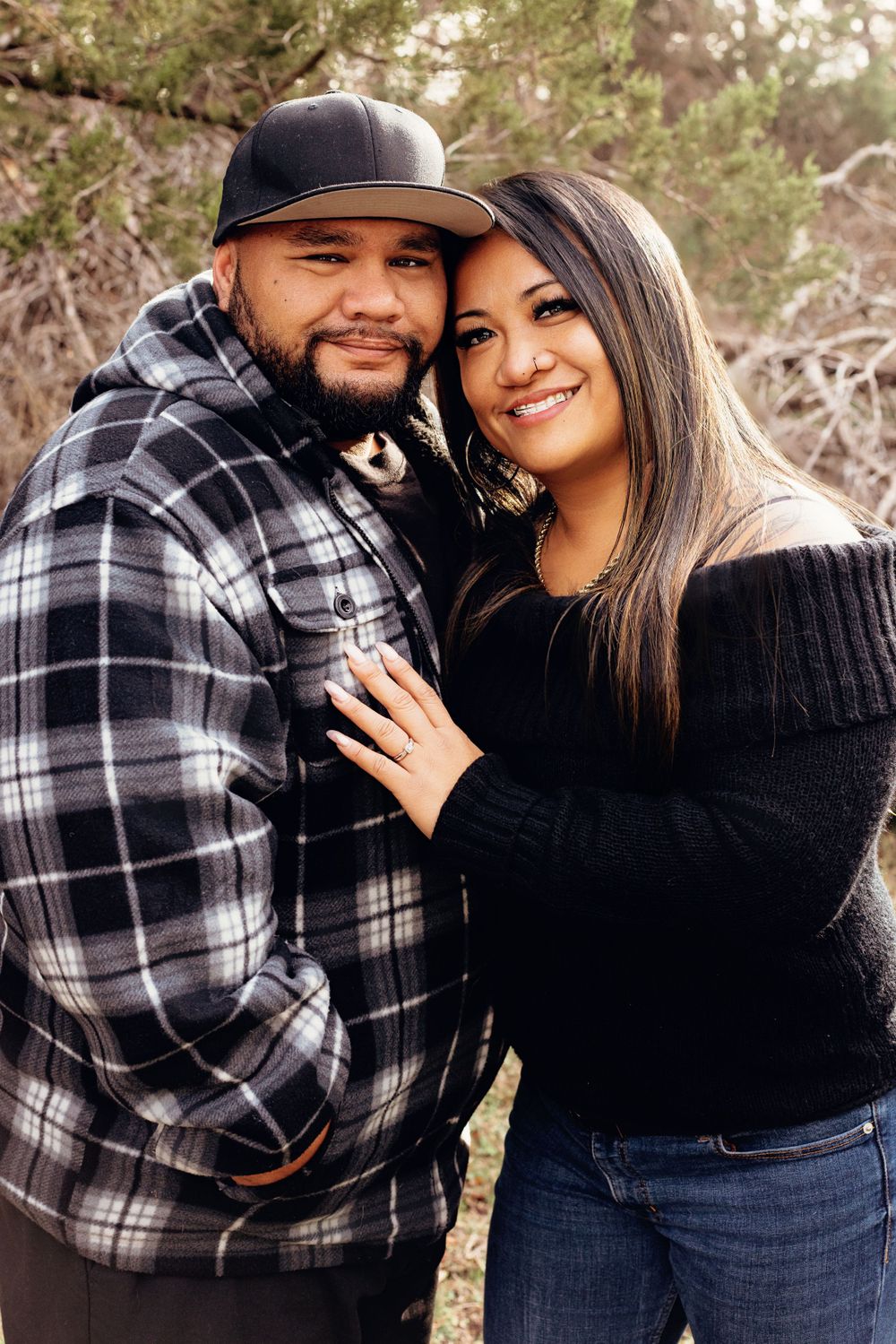 A couple in plaid and black clothing smiles together during an outdoor photo session.