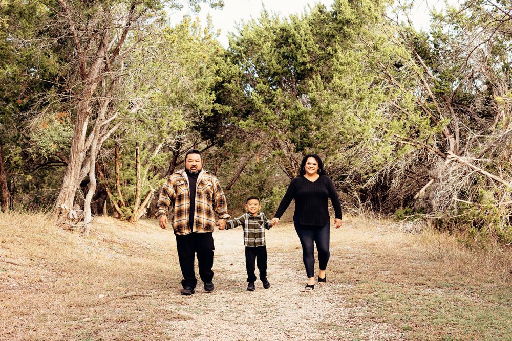 Three people walking together and holding hands on a dirt path surrounded by trees and brush in a natural setting.