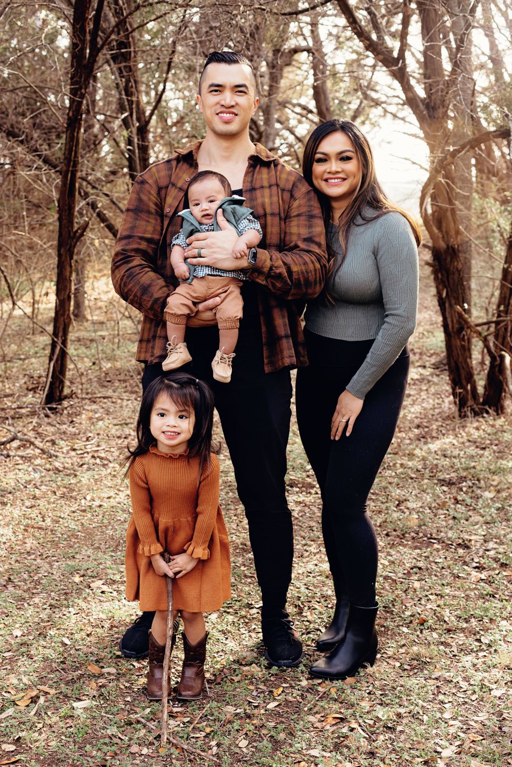 A young family of four poses together in a forest setting during fall.