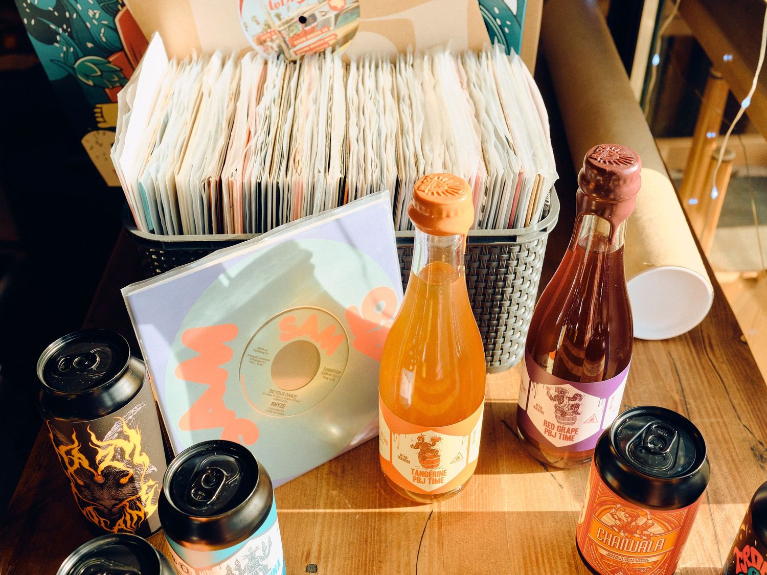 A collection of vinyl records, beverages and glass bottles arranged on a wooden table surface.