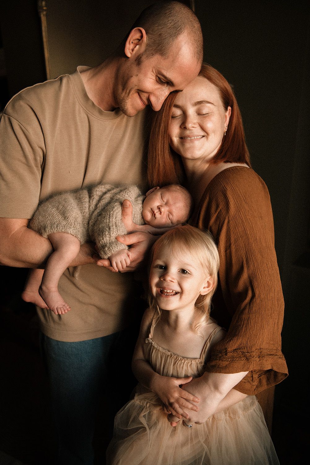 A family shares tender moments together in a series of dark moody portraits against a black background.