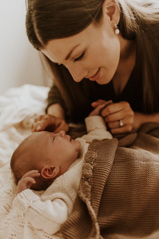 A tender intimate moment of love between parent and newborn baby in soft sweaters with warm natural lighting.