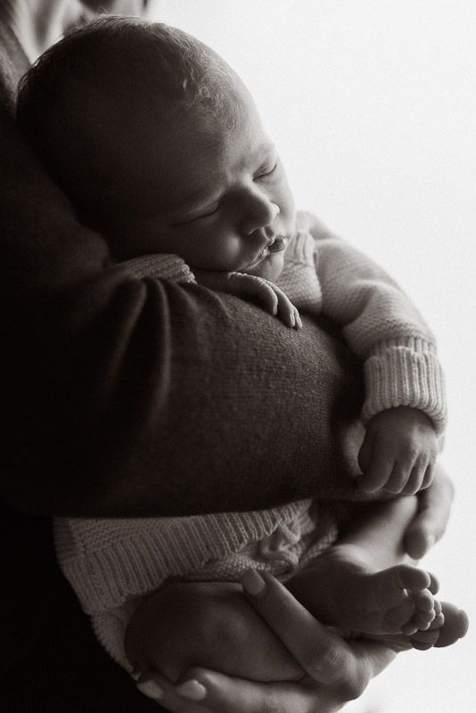 Intimate black and white portrait of a sleeping infant being cradled in soft sweater-clad arms.