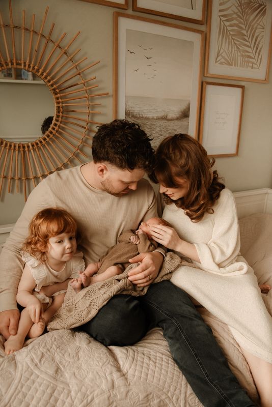 A family shares tender moments together while relaxing on a cozy bed with neutral tones and sunlit decor.