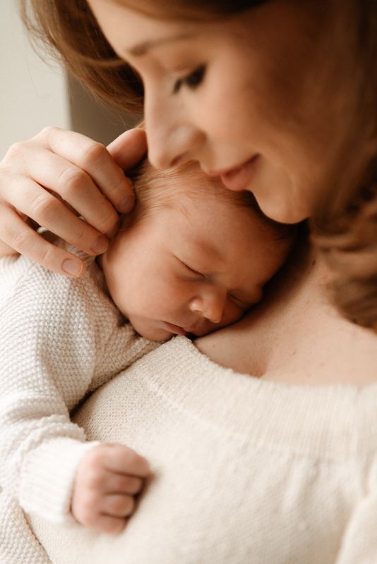 Close-up images of tender moments between parent and baby in soft, warm lighting with white knit clothing.