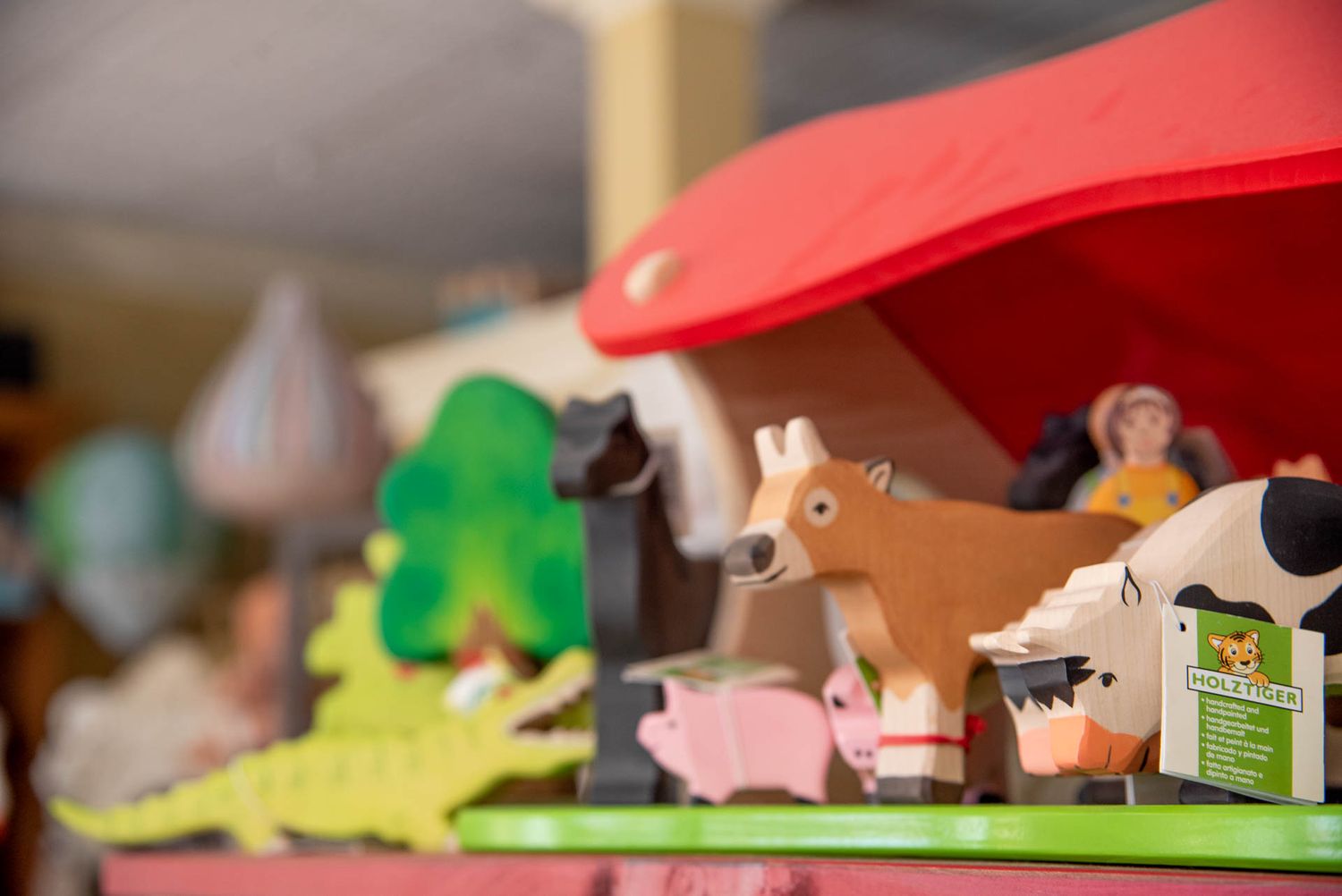 A collection of wooden toy farm animals including a cow, horse, and pig arranged under a red barn roof structure.