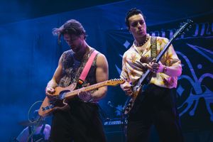 Two guitarists performing on stage under blue and pink lights at a live concert.