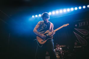 Guitarist performing on stage under blue lights at a live music venue, playing a Telecaster guitar.