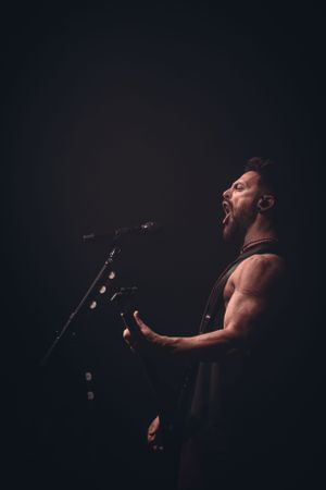 Concert performer singing passionately on stage in dramatic low-key lighting.