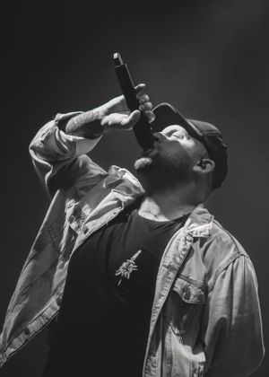 Black and white portrait of a performer singing intensely into a microphone on stage.