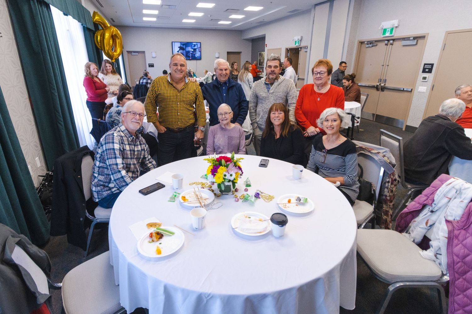 Group gathered around a white circular table in a community room for a social gathering or celebration.