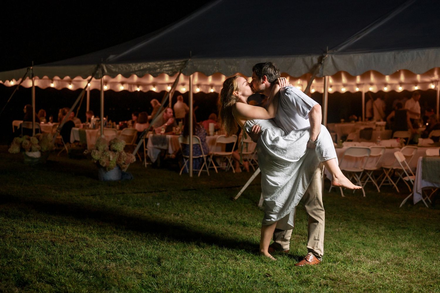 Wedding reception guests dancing under string lights at an outdoor evening celebration.