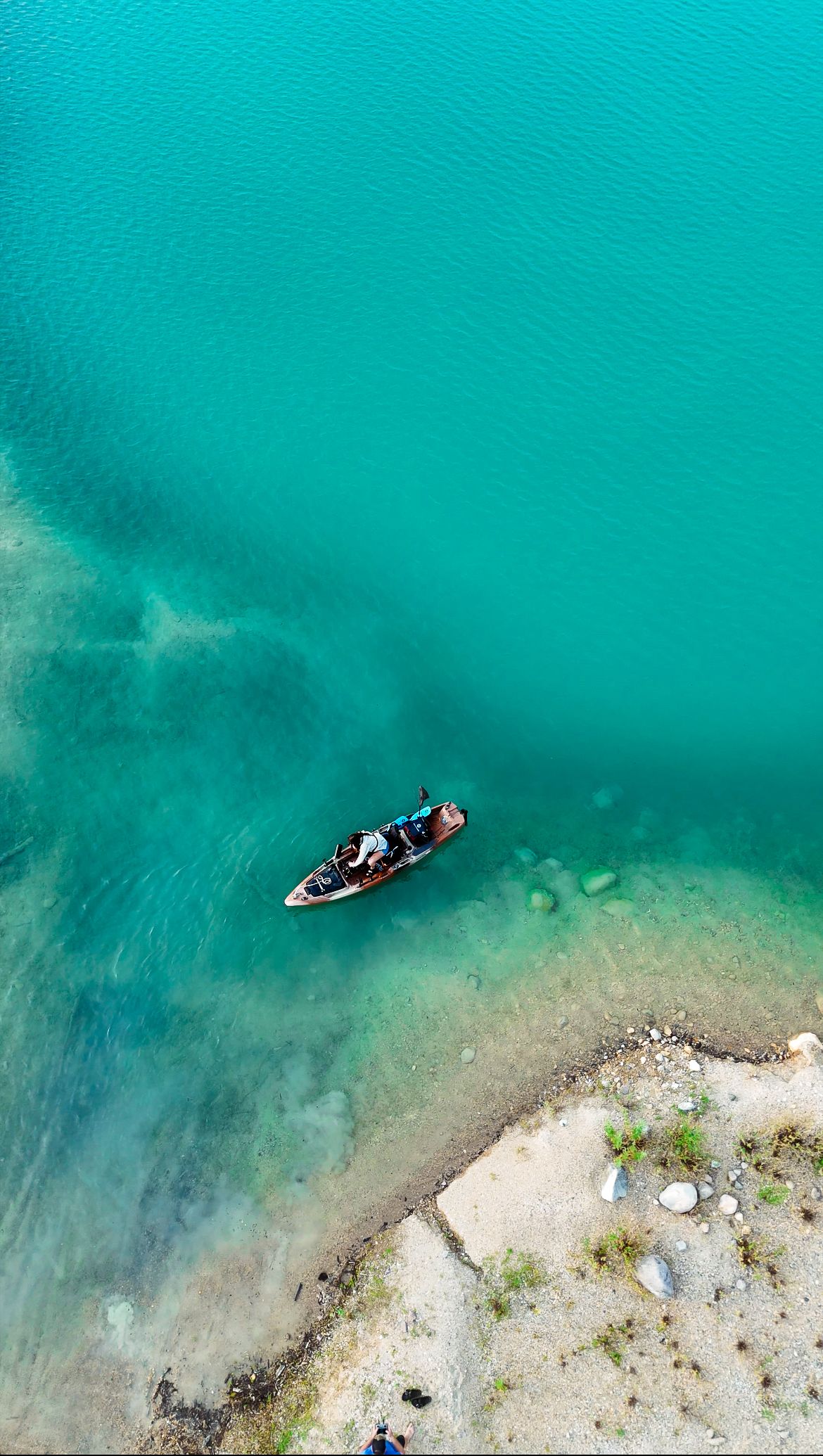 Aerial view of a small boat floating in crystal clear turquoise waters near a rocky shoreline.