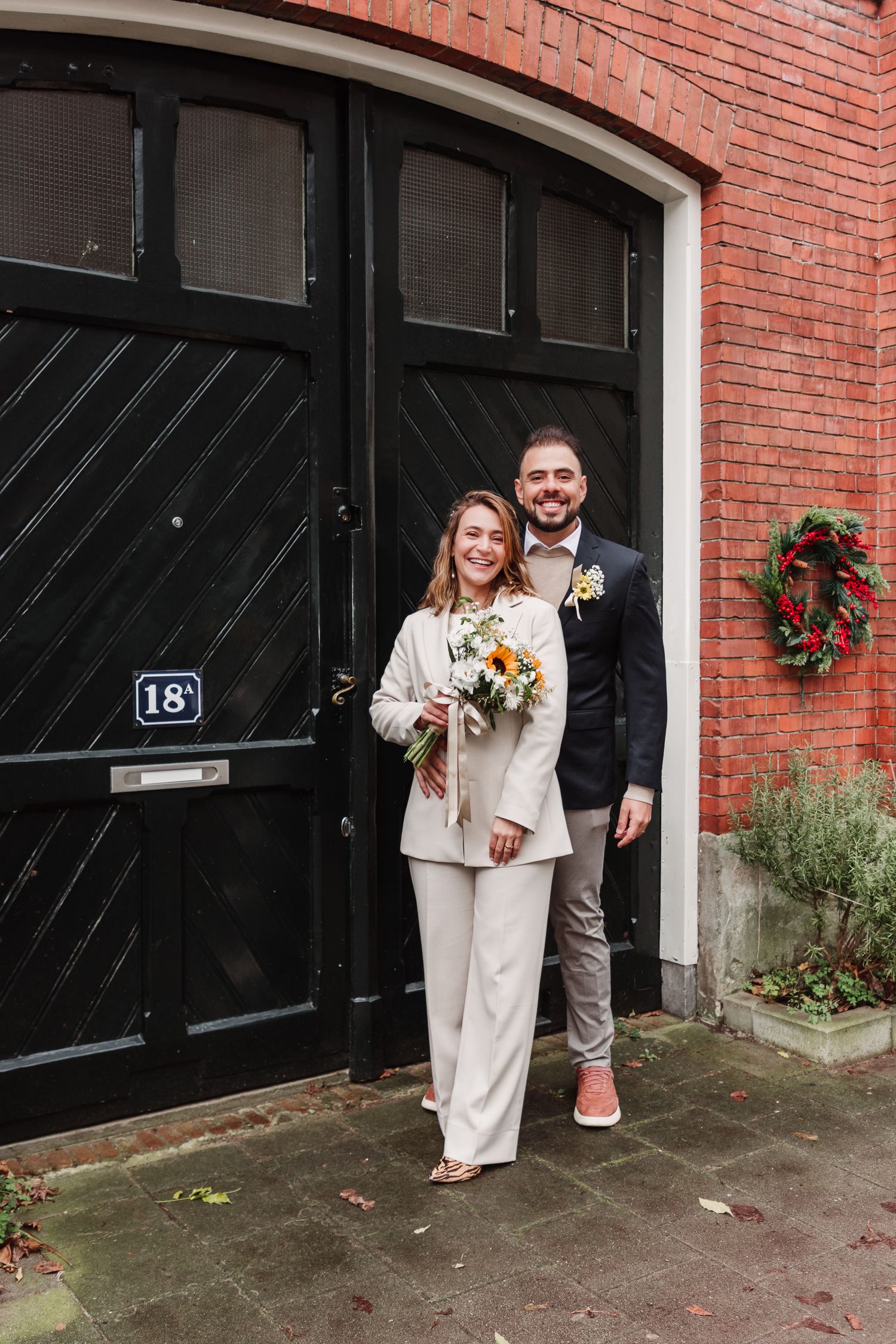 Newlywed couple posing in front of typical Amsterdam brick house after their gemeente wedding in Amsterdam