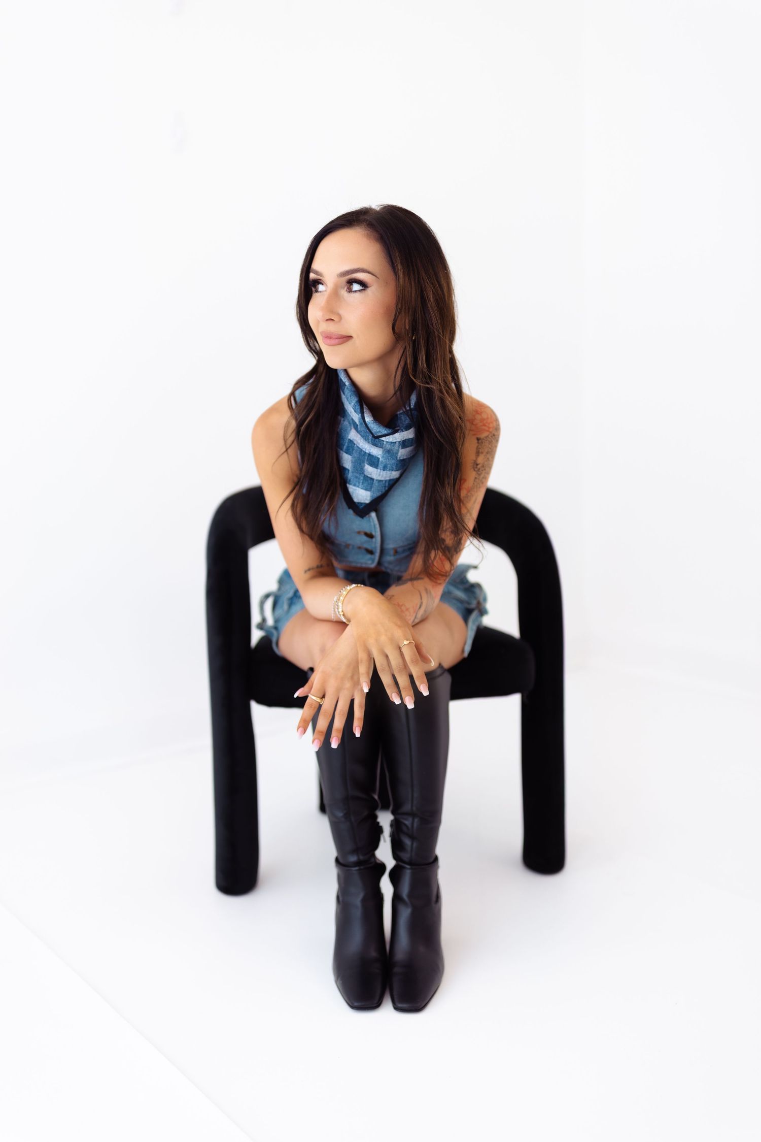 Stylish portrait shot on a black chair against white background featuring blue scarf and black boots.