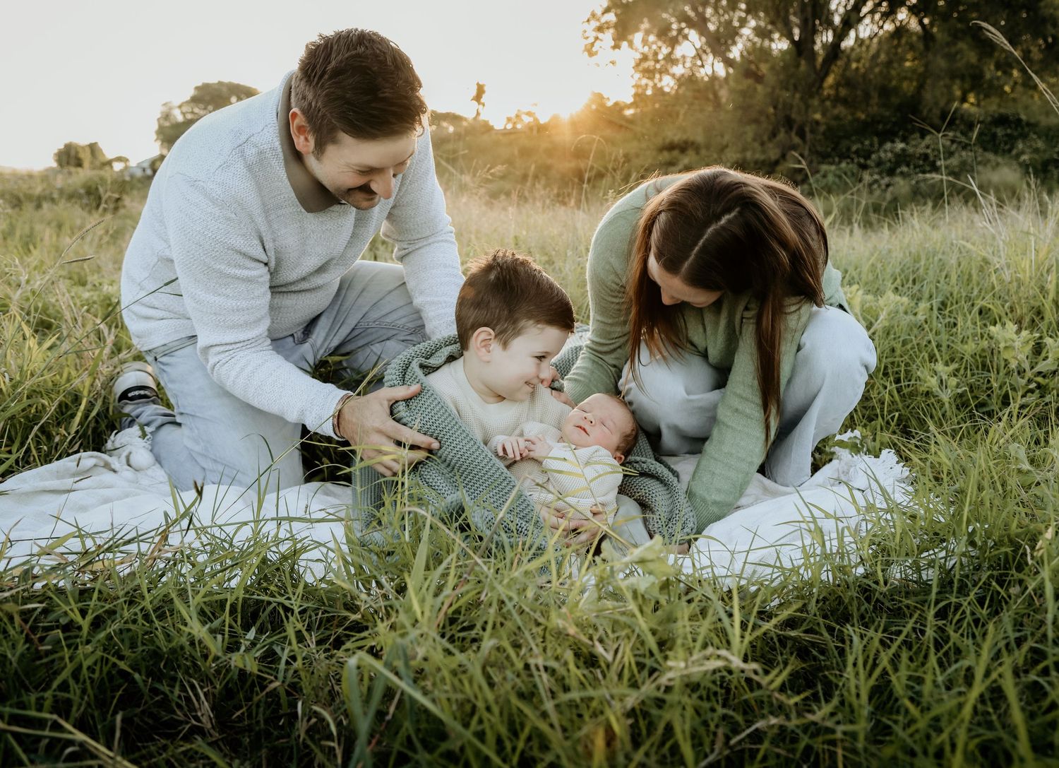 A family cuddling with a blanket outside