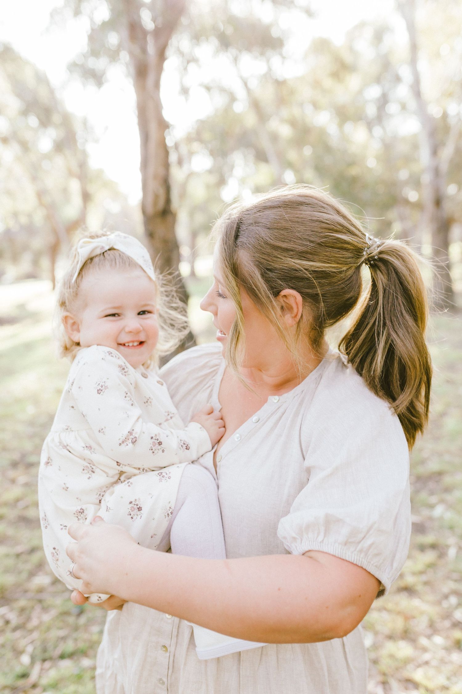 A tender family moment captured outdoors showing a parent holding and interacting with their baby in a sunlit garden setting.