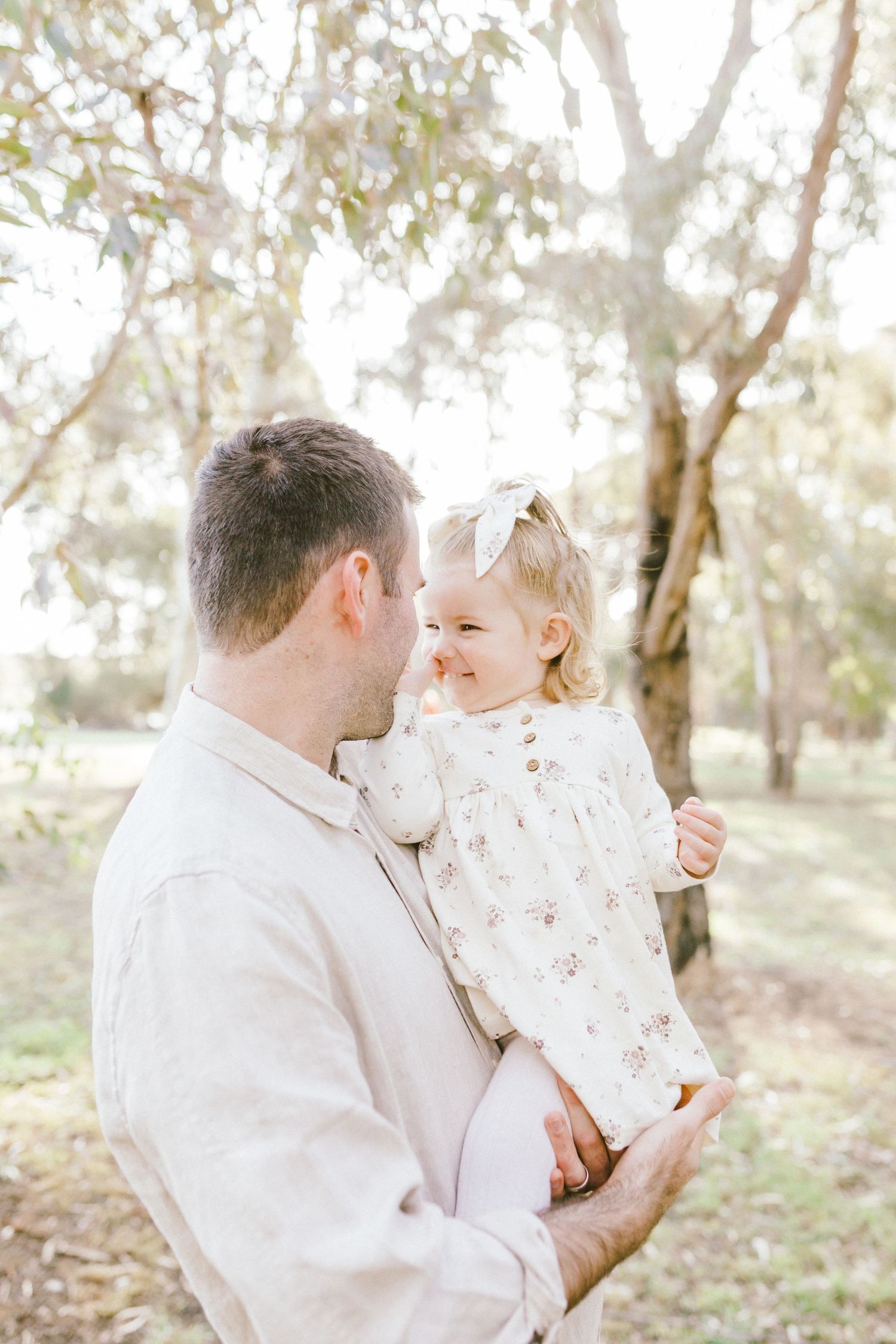 A tender moment captured between parent and child wearing white lace against a soft sunlit woodland backdrop.