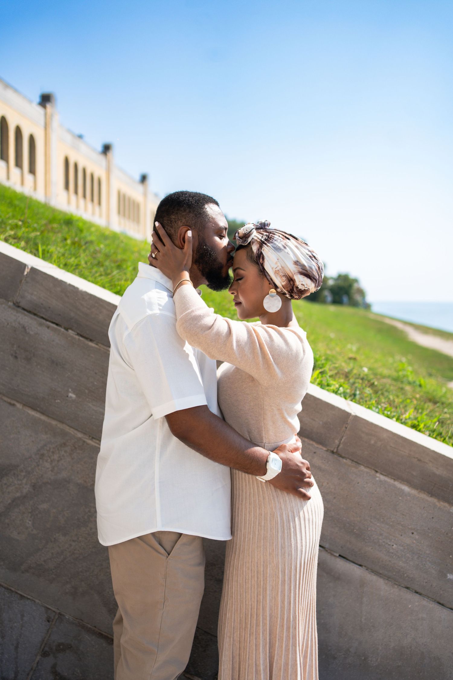 Romantic engagement photoshoot on hillside with couple in neutral toned outfits.