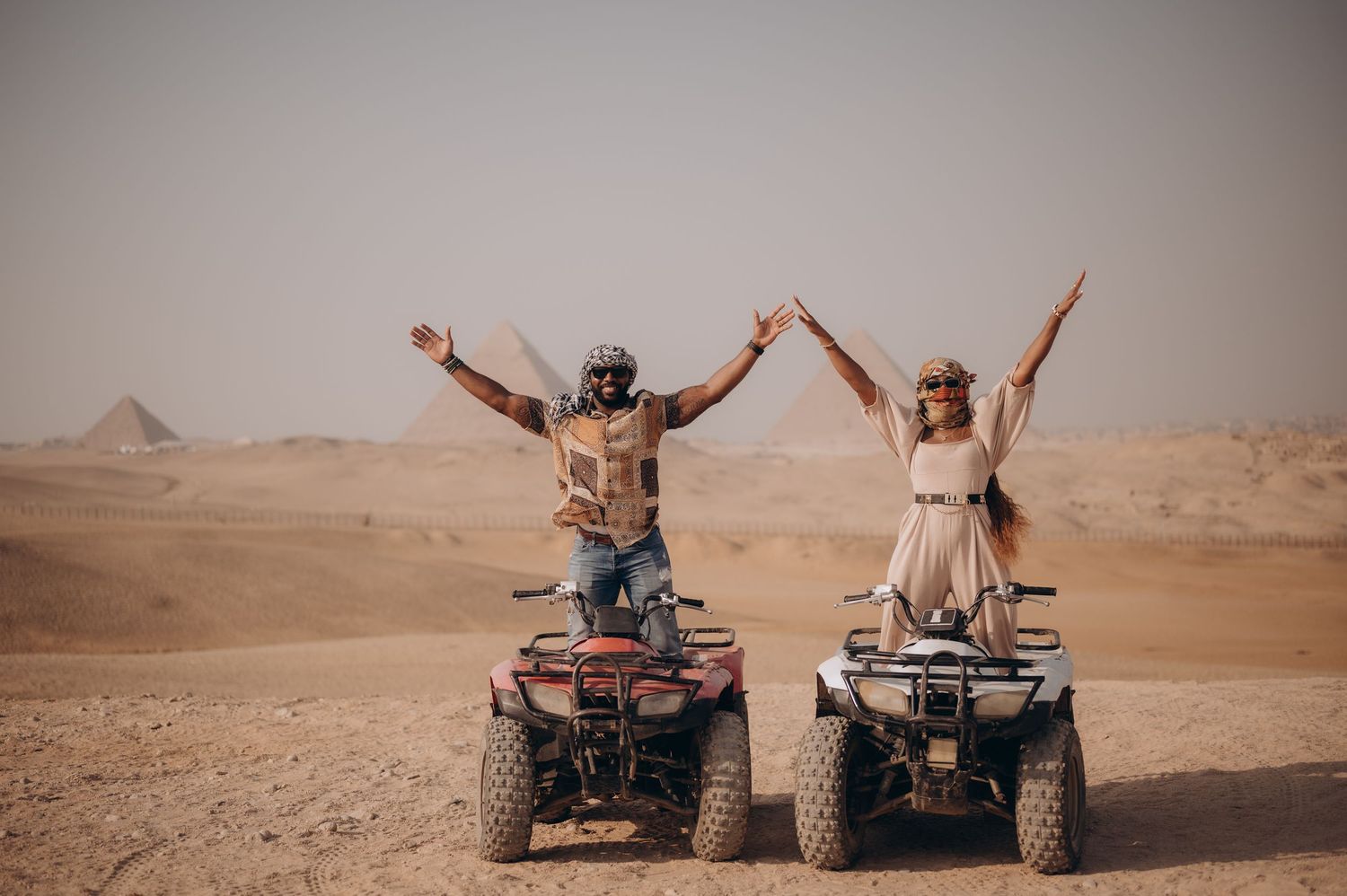 Adventure seekers riding ATVs in the desert with pyramids visible in the background.