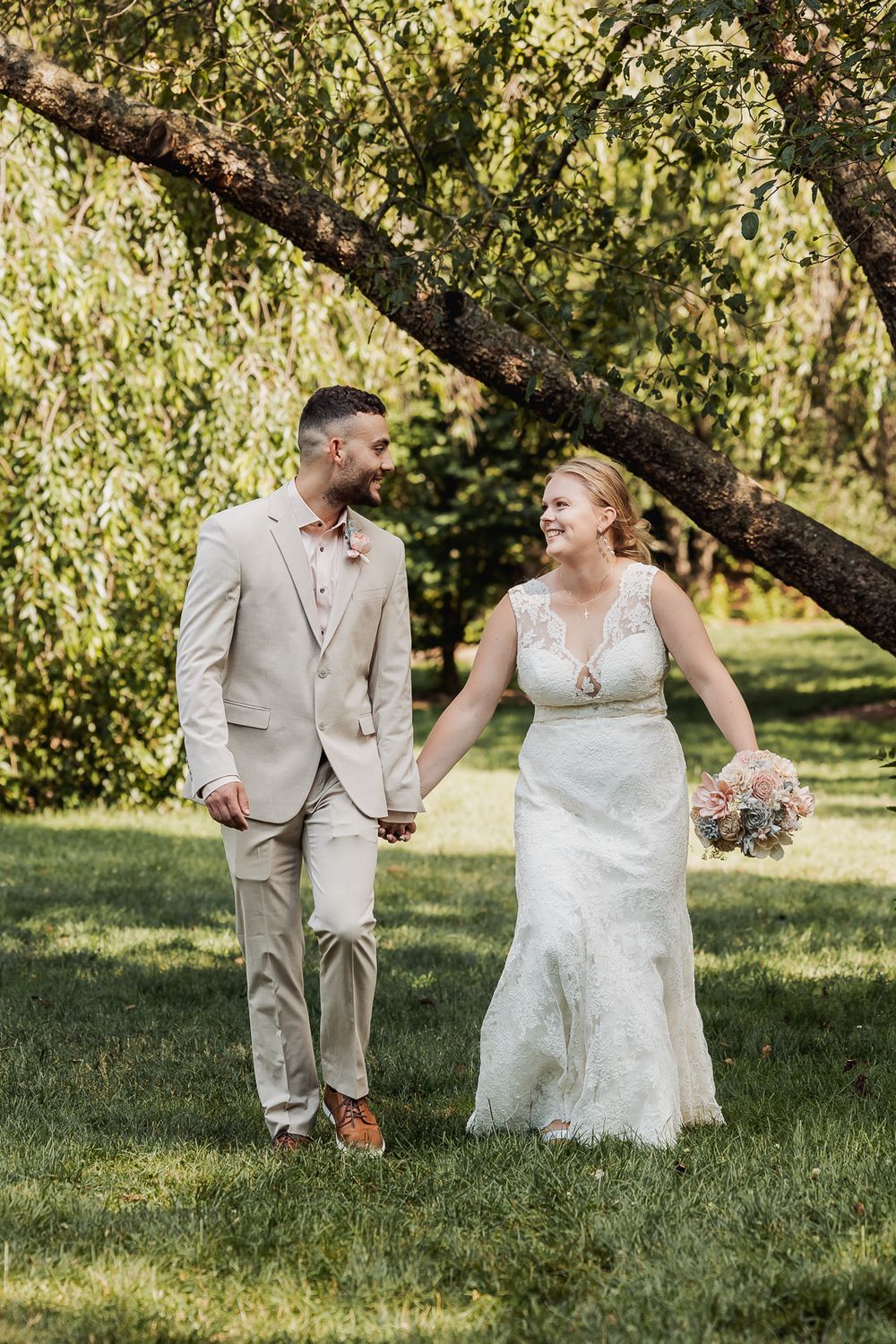 A couple in wedding attire shares joyful moments together in a sun-dappled orchard setting during their special day.