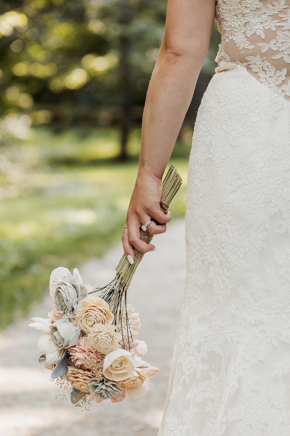 Bride in a white lace dress holds a delicate dried flower bouquet featuring roses and other preserved blooms.