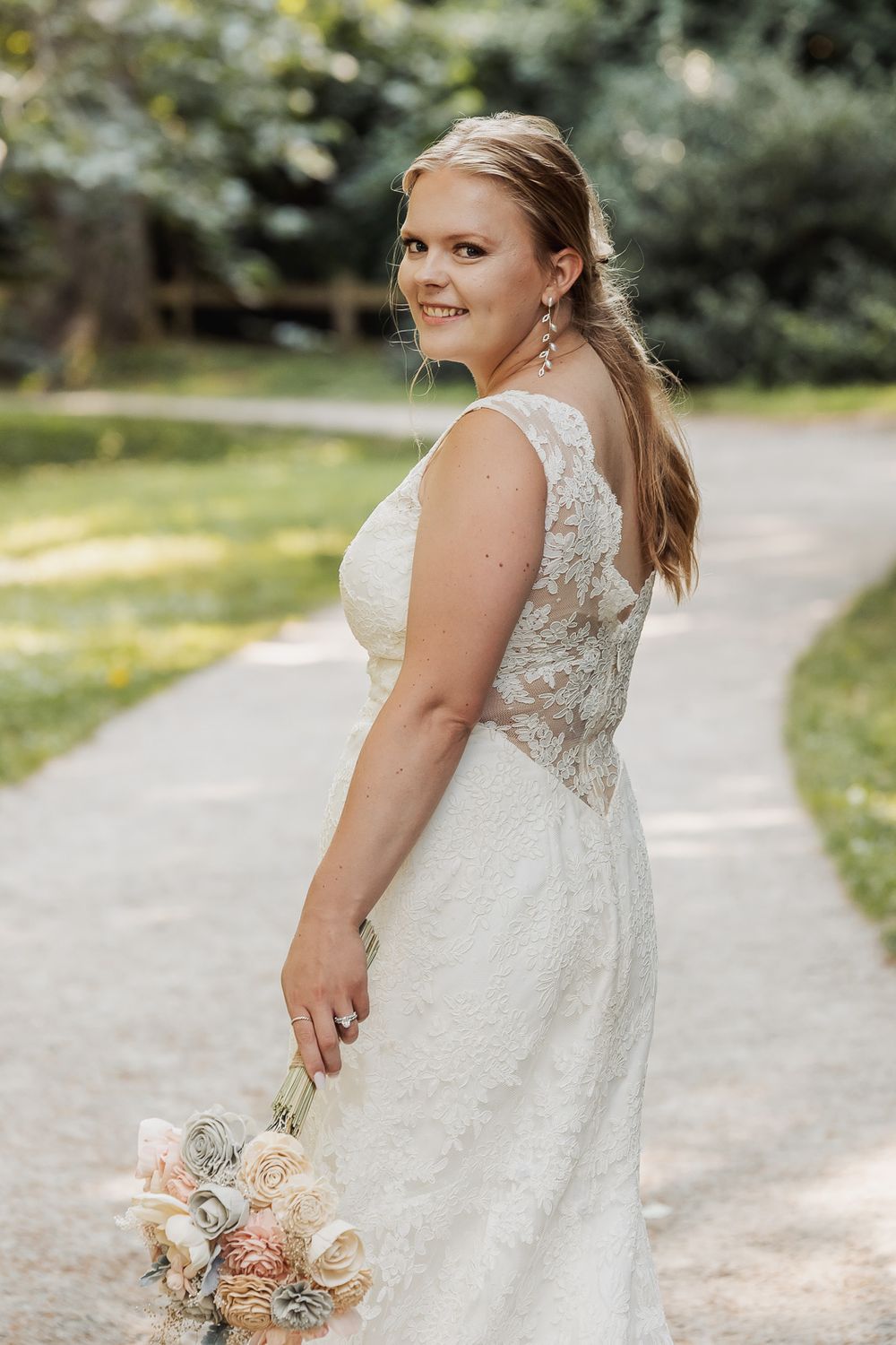 Delicate lace wedding dress with fitted bodice photographed in a sunlit garden setting.
