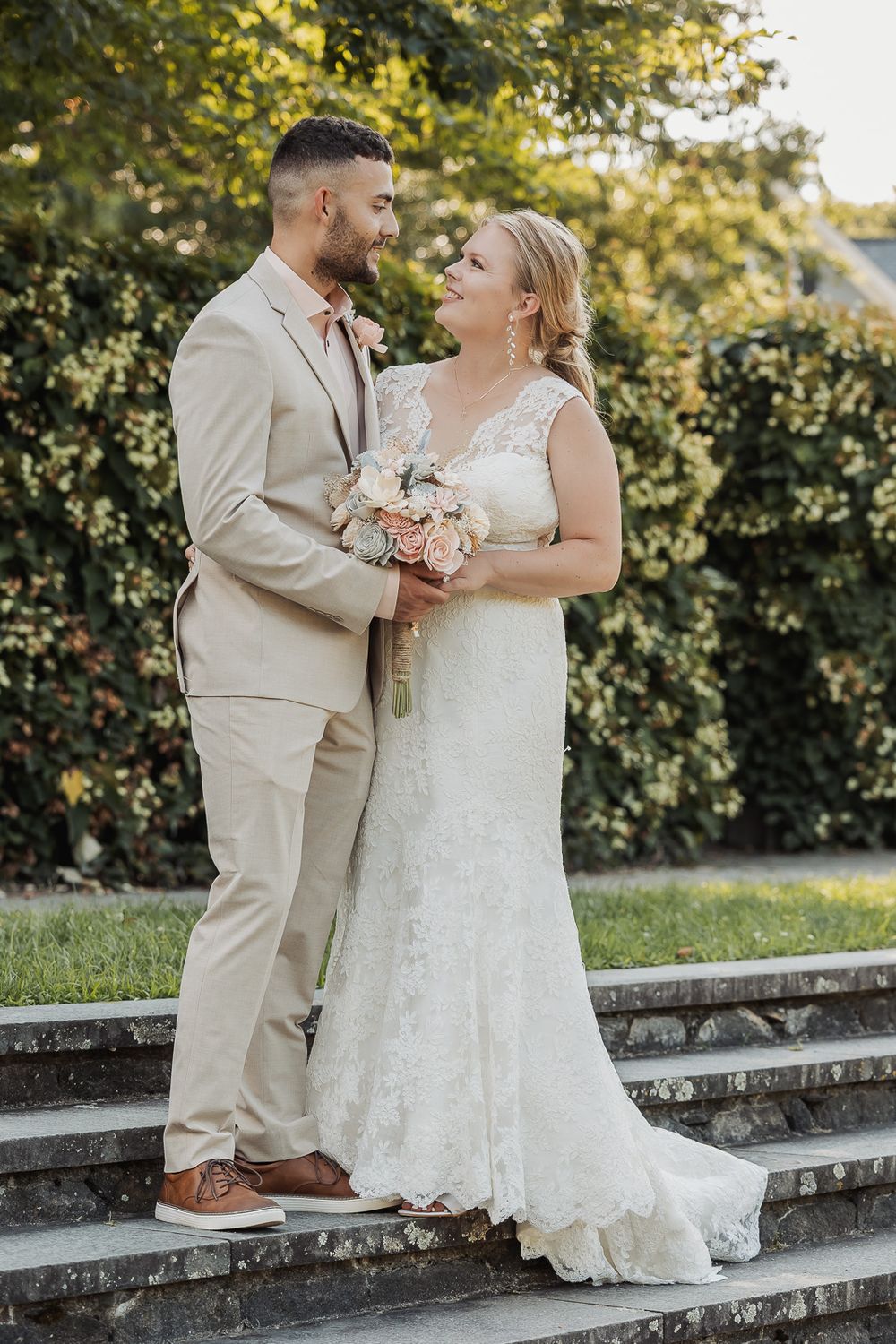 A couple shares romantic wedding photos on stone steps surrounded by greenery on their special day.