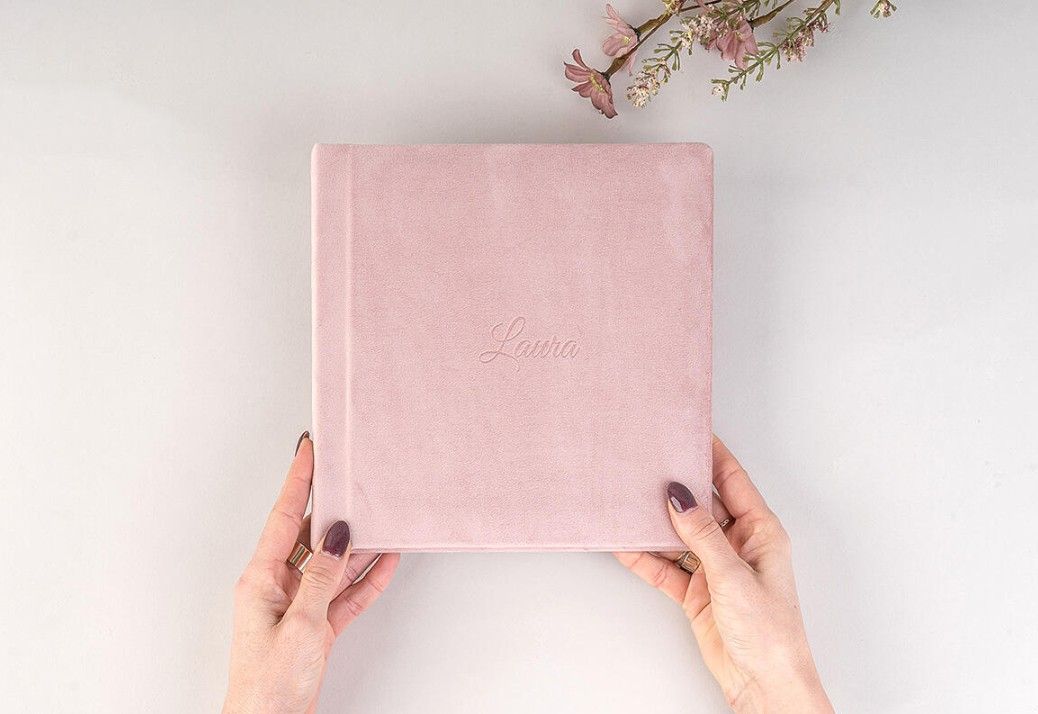 Hands hold various dusty pink and rose-colored artist sketchbooks or notebooks against a light background.